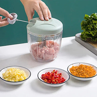 Hand operating manual food chopper with minced meat inside, surrounded by bowls of chopped garlic, red chili, and orange spices